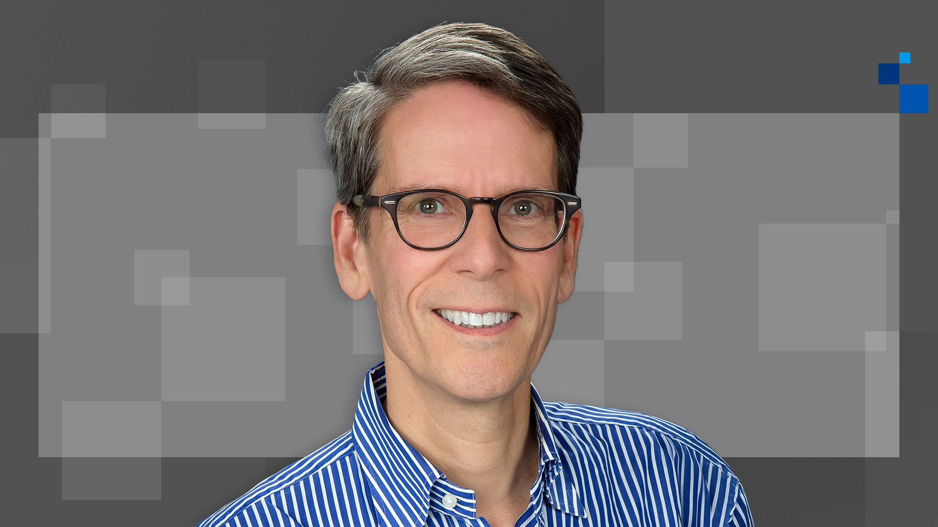 A person with short, graying hair wears glasses and smiles at the camera. They are dressed in a blue and white striped shirt. The background features a geometric pattern with various shades of gray and small blue squares.